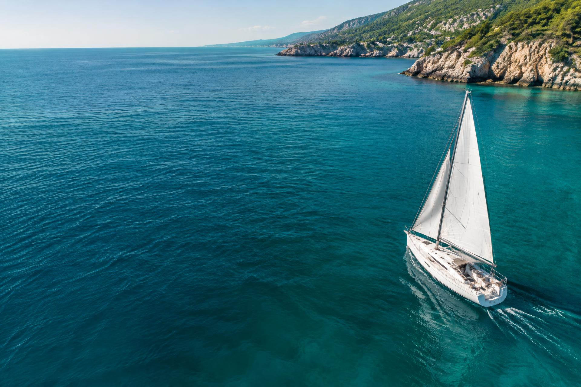 Segelboot auf türkisblauem Meer vor einer grünen Küste